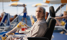 A battered-looking white man (Joaquin Phoenix) sits in an airline seat amidst people in pool chairs.