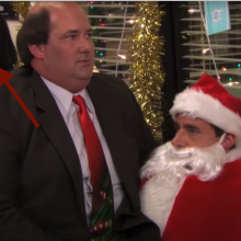 A man sitting on the lap of a man dressed as Santa Claus. An arrow points to a woman laughing in the background.