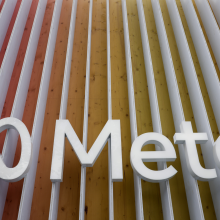 The Meta logo sign in front of a building. The log is white, the building is covered in white lines, interspersed with red, orange, and yellow lines.