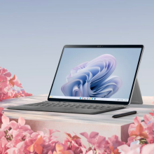 the microsoft surface pro 9 with a keyboard and a pen on a cream-colored surface amid beds of pink flowers