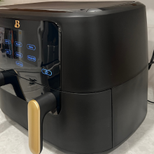 black air fryer with two gold handles and lit-up LED touch panel