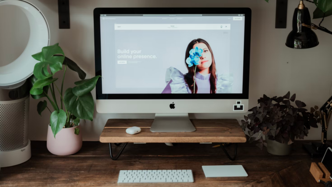 squarespace's website pulled up on an imac sitting on a wooden desk that's surrounded by plants