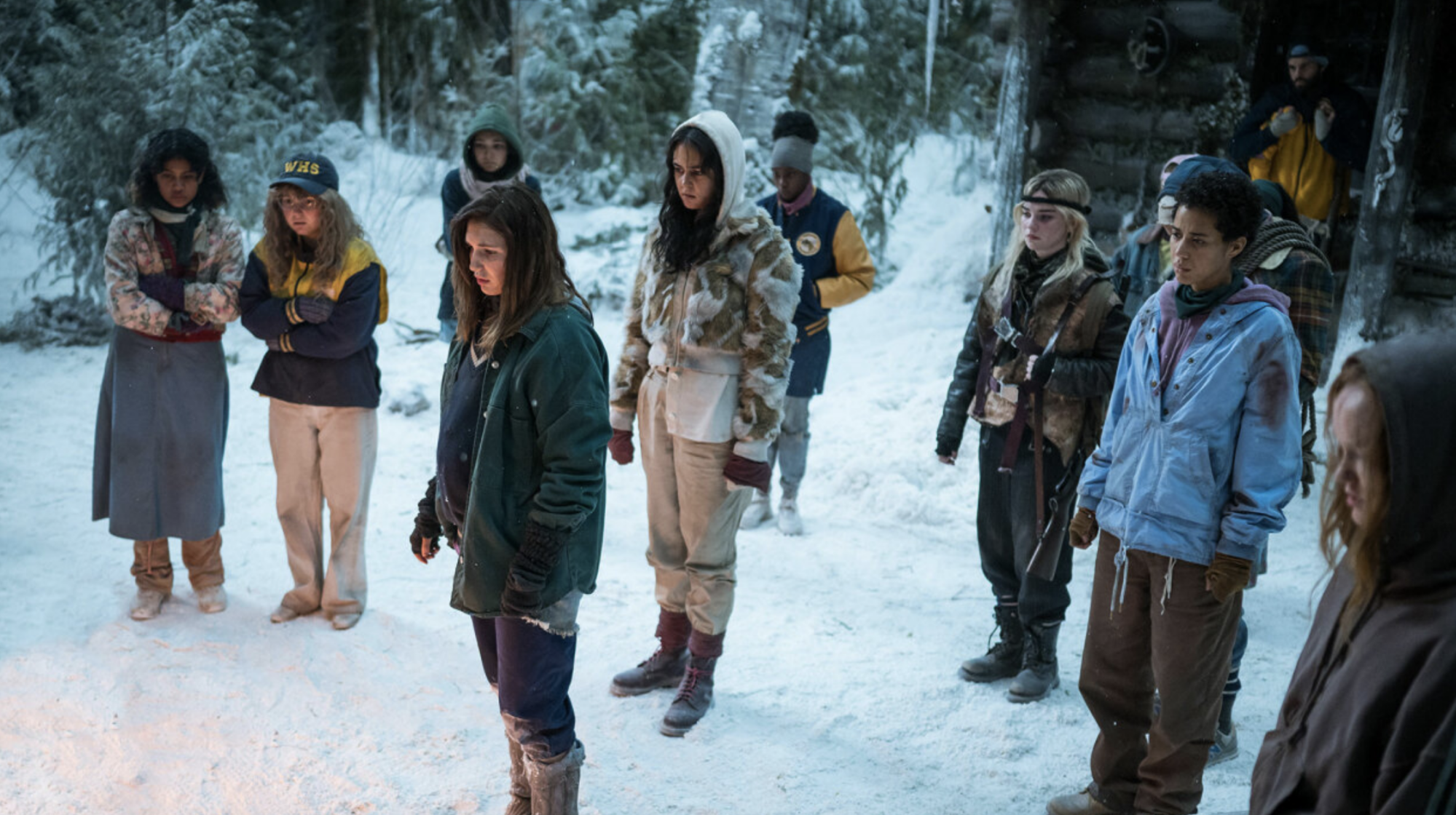 A group of girls stand in the snowy wilderness outside a cabin.