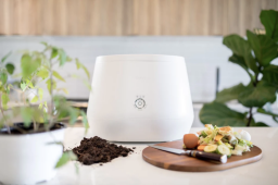 Lomi composter on countertop with food scraps, fertilizer, and plants