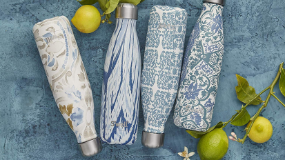 Four water bottles with different patterns on blue surface with a couple limes