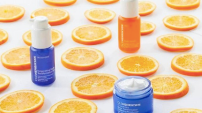 Orange slices on surface with an orange bottle, a blue bottle, and a blue tub of skincare 