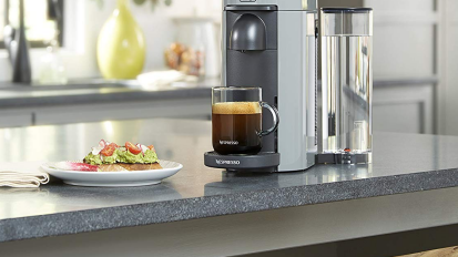 Black and grey coffee maker with cup of coffee under it next to plate of avocado toast