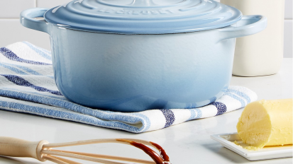 Blue dutch oven on towel behind chocolate-covered whisk and dish of butter