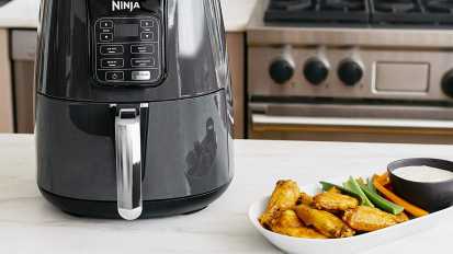 black air fryer next to plate of wings and veggies