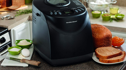 Black bread maker on kitchen counter sandwiched by loaf of bread and bread ingredients